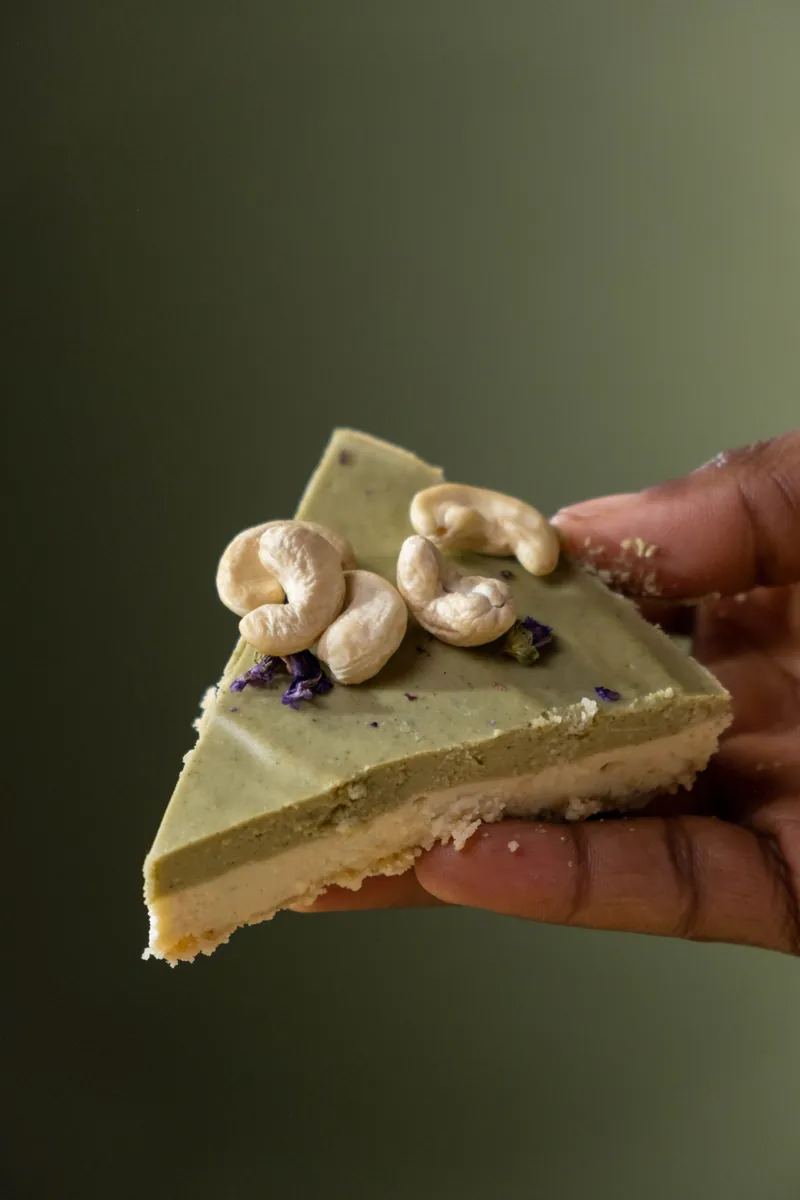 Hand holding a slice of lime and cashew cream cake